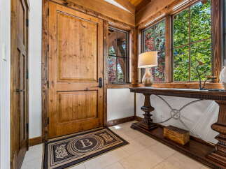 Step into a warm and inviting entryway featuring a rustic wooden door and a large window overlooking lush greenery.