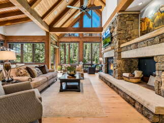 Experience luxury mountain living in this stunning great room, featuring a soaring vaulted ceiling with exposed wooden beams and a grand stone fireplace.