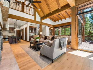 Experience luxurious mountain living in this stunning great room, featuring a soaring vaulted ceiling with exposed wooden beams and a grand stone fireplace.