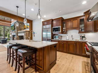 Experience luxury mountain living in this stunning kitchen, featuring rich cherry wood cabinetry, a spacious granite island with seating, and a professional-grade stainless steel range.