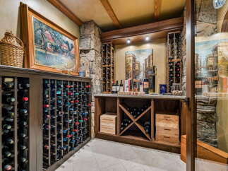 Discover this exquisite wine cellar, featuring a vast collection of wine racks filled with bottles, complemented by rustic stone accents and warm wooden beams.