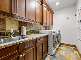 This laundry room boasts beautiful dark wood cabinetry with granite countertops, complemented by a slate tile backsplash.