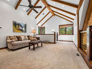 Experience rustic charm in this spacious living area, featuring a vaulted ceiling with exposed wooden beams and a stylish ceiling fan.