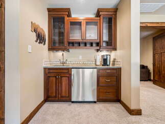This charming wet bar features rich wooden cabinetry, a sleek stainless steel mini-fridge, and a granite countertop perfect for entertaining.