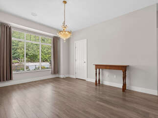 This spacious room features a large bay window with blinds and elegant drapery, offering a view of lush greenery.
