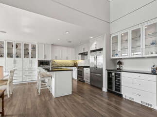 This spacious kitchen boasts ample white cabinetry, including glass-front display cabinets and a large island with seating.