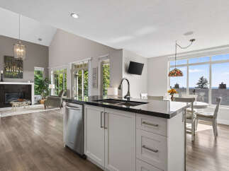 Experience open-concept living with this stunning kitchen and living area, featuring a vaulted ceiling and a modern fireplace.