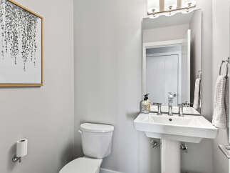 This modern powder room features a sleek white pedestal sink with chrome fixtures, complemented by a decorative soap dispenser and a framed botanical print on the wall.