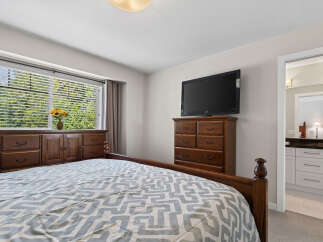 This inviting bedroom features a spacious wooden dresser and a mounted television for entertainment.