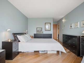 This spacious bedroom features a comfortable queen-size bed with crisp white linens, complemented by two dark wood nightstands.