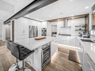 Experience modern luxury in this stunning white high-gloss kitchen, featuring a spacious island with a built-in wine cooler and sleek bar stools.