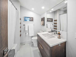 This modern bathroom features a sleek dark wood vanity with a white quartz countertop, complemented by a minimalist white sink and a wall-mounted faucet.