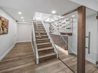 Experience sophisticated living with this stunning modern home featuring a sleek glass-enclosed wine cellar adjacent to a beautifully crafted wooden staircase.