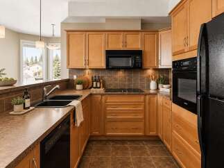 This kitchen boasts beautiful light wood cabinetry complemented by a rich brown tiled backsplash and countertops.