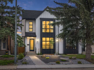 Discover modern living in this stunning two-story home featuring a striking black and white facade with large, black-framed windows that illuminate the interior with warm light.