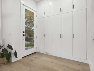 This entryway features a wall of floor-to-ceiling white cabinets with sleek black hardware, offering ample storage.