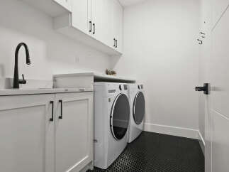 This modern laundry room features sleek white cabinetry with black hardware, a stylish black faucet over a white sink, and matching LG washer and dryer units.