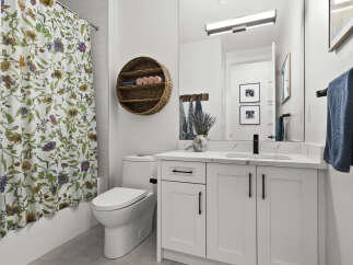 This modern bathroom features a white vanity with a marble countertop and black hardware, complemented by a floral shower curtain and a round woven shelf.