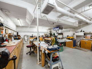 This spacious workshop is equipped with a variety of woodworking tools and machinery, including a table saw, miter saw, and a robust workbench with a vise.