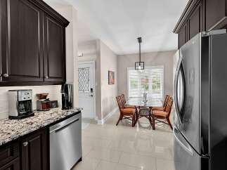 This kitchen features dark wood cabinetry and a granite countertop, complemented by a stainless steel coffee maker and dishwasher.