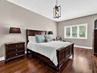 Experience luxury and comfort in this master bedroom, featuring a spacious dark wood bed frame adorned with plush pillows and a white comforter.