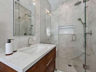 Experience modern luxury in this stunning bathroom, featuring a sleek vanity with a quartz countertop and a spacious glass-enclosed shower with marble-look tiles.