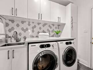 This modern laundry room features sleek white cabinetry, a stylish hexagonal tile backsplash, and a convenient undermount sink.