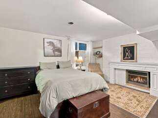 Cozy bedroom featuring a comfortable bed with plush bedding, a dark wood dresser, and a decorative fireplace with a gold-framed artwork above.