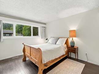 Discover comfort and style in this inviting bedroom, featuring a charming wooden bed frame and a large window offering serene views of lush greenery.