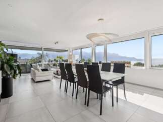 Experience luxurious living in this modern dining and living area, boasting panoramic views of the serene lake and majestic mountains through expansive floor-to-ceiling windows.