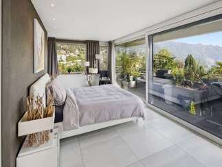 Experience luxurious living with this stunning bedroom featuring a king-sized bed and breathtaking panoramic views of the mountains and lake.
