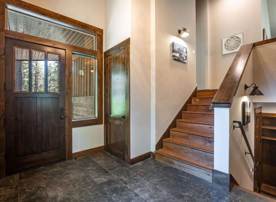 Step into a warm and inviting entryway featuring a rustic wooden door with glass panels, offering a glimpse of the natural beauty outside.