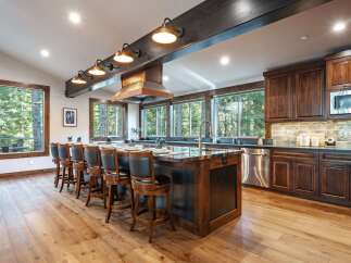 Experience luxury mountain living in this stunning kitchen, featuring a large granite island with bar seating and a copper range hood.