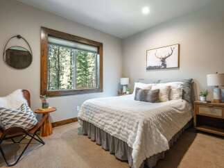 Experience serene mountain living in this charming bedroom, featuring a large window with picturesque forest views.