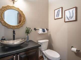 This stylish bathroom features a unique hammered metal vessel sink atop a dark granite countertop, complemented by a decorative gold-framed mirror.