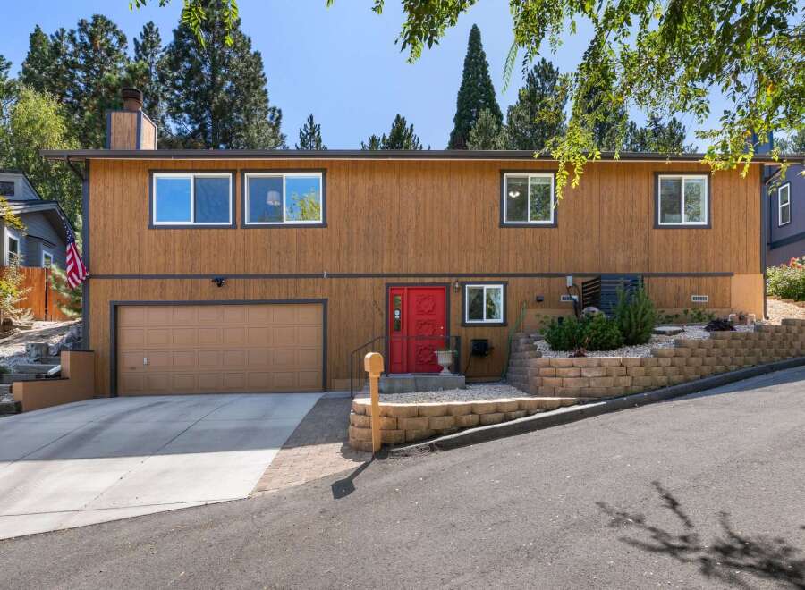 Discover this charming home featuring a warm wood exterior and a striking red front door, creating an inviting entryway.