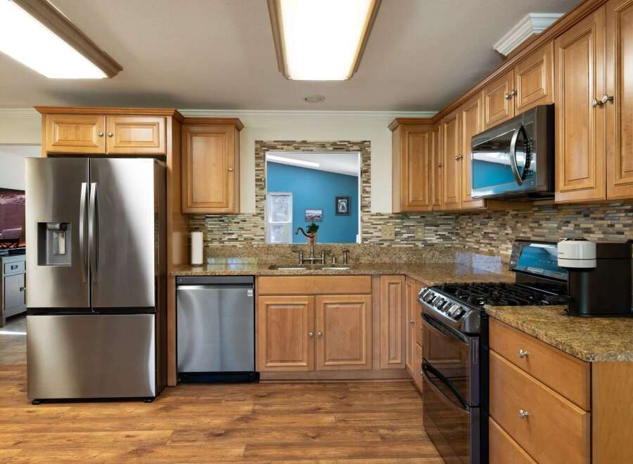 This spacious kitchen features beautiful light wood cabinetry, granite countertops, and a stylish mosaic tile backsplash.