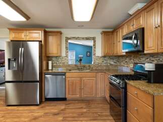 This spacious kitchen features beautiful light wood cabinetry, granite countertops, and a stylish mosaic tile backsplash.
