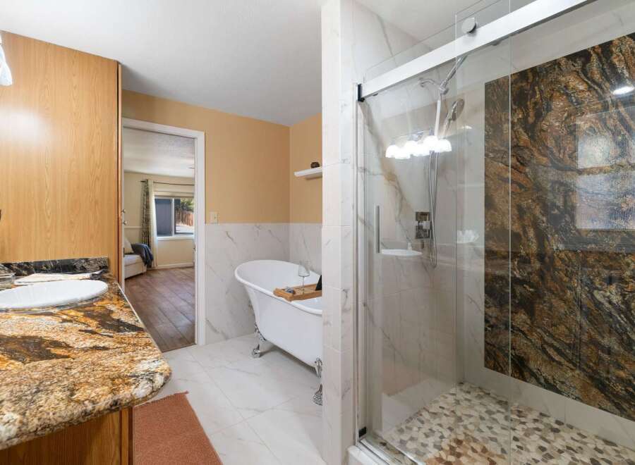 Indulge in luxury with this stunning bathroom featuring a freestanding clawfoot tub and a spacious walk-in shower with a dramatic granite accent wall.