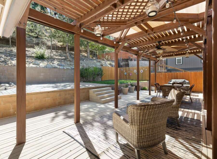 Enjoy outdoor living under this expansive wooden pergola, complete with ambient string lights and a ceiling fan for ultimate comfort.
