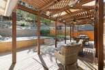 Enjoy outdoor living under this expansive wooden pergola, complete with ambient string lights and a ceiling fan for ultimate comfort.