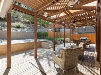 Enjoy outdoor living under this expansive wooden pergola, complete with ambient string lights and a ceiling fan for ultimate comfort.