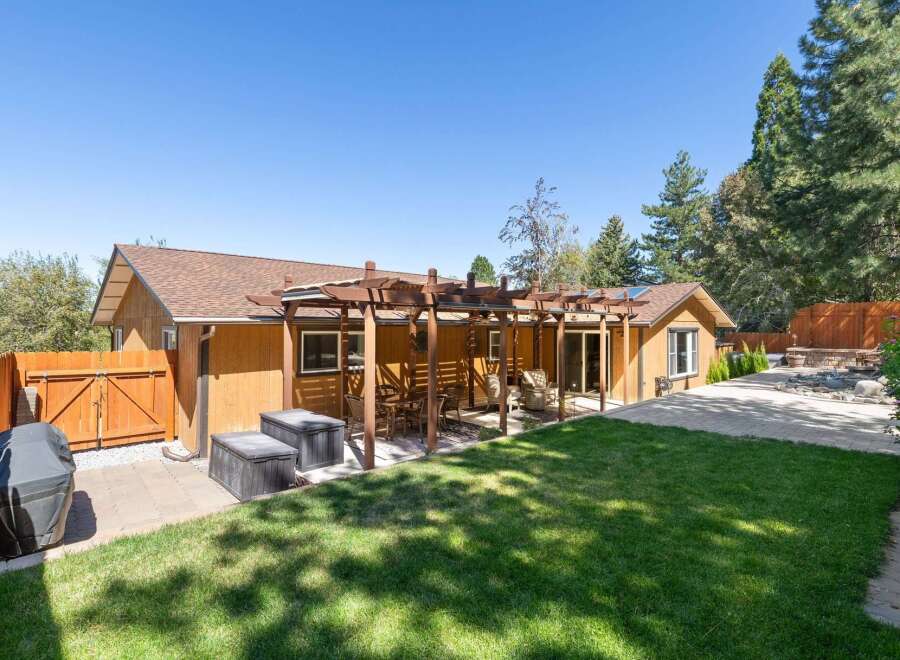 Enjoy outdoor living with this charming backyard featuring a spacious wooden pergola perfect for al fresco dining and relaxation.