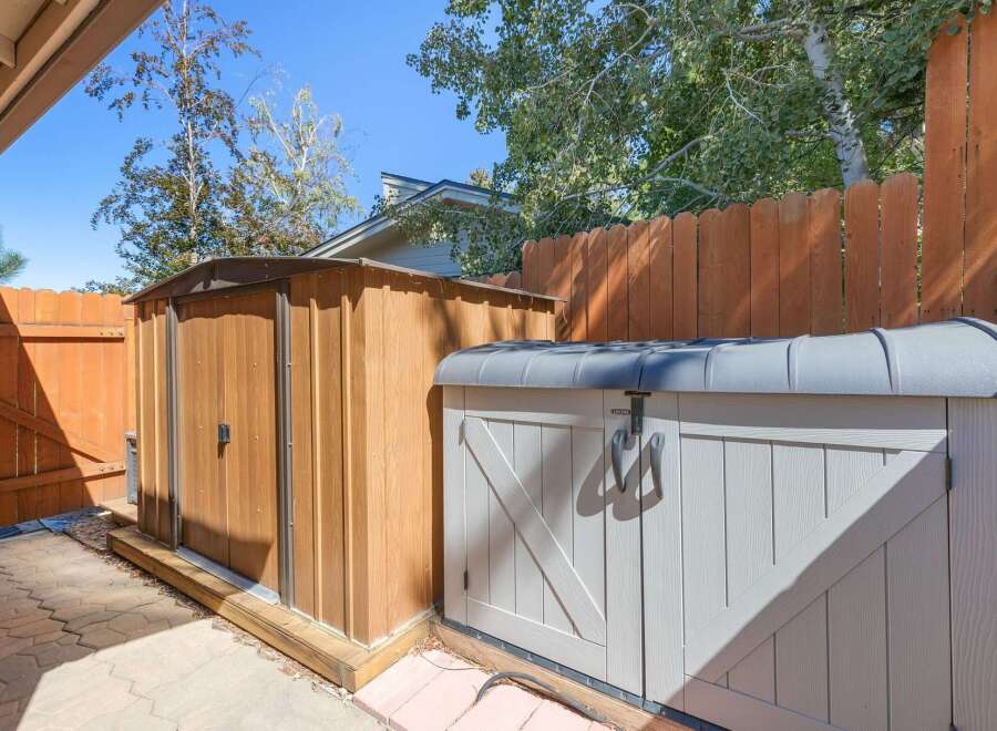 Enhance your outdoor storage with this practical setup, featuring a tall wooden shed and a complementary grey storage unit.