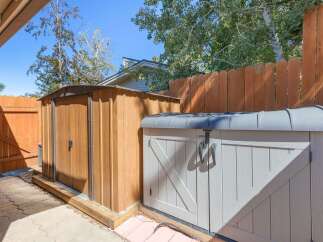 Enhance your outdoor storage with this practical setup, featuring a tall wooden shed and a complementary grey storage unit.