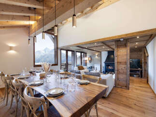 Experience luxurious mountain living in this stunning dining and living area, featuring a grand wooden dining table set for a feast and a cozy fireplace perfect for après-ski relaxation.