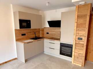 Discover this modern L-shaped kitchen featuring sleek, light-colored cabinetry and a wood-effect backsplash.
