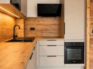 Discover this modern kitchen featuring a sleek black sink and faucet, complemented by warm wooden countertops and backsplash.