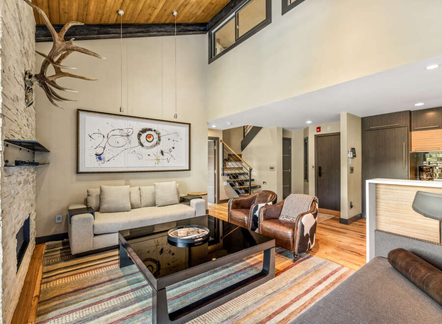 Experience luxury mountain living in this stunning great room, featuring a soaring vaulted ceiling with exposed wood beams and a dramatic stone fireplace adorned with impressive antlers.