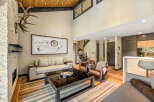 Experience luxury mountain living in this stunning great room, featuring a soaring vaulted ceiling with exposed wood beams and a dramatic stone fireplace adorned with impressive antlers.